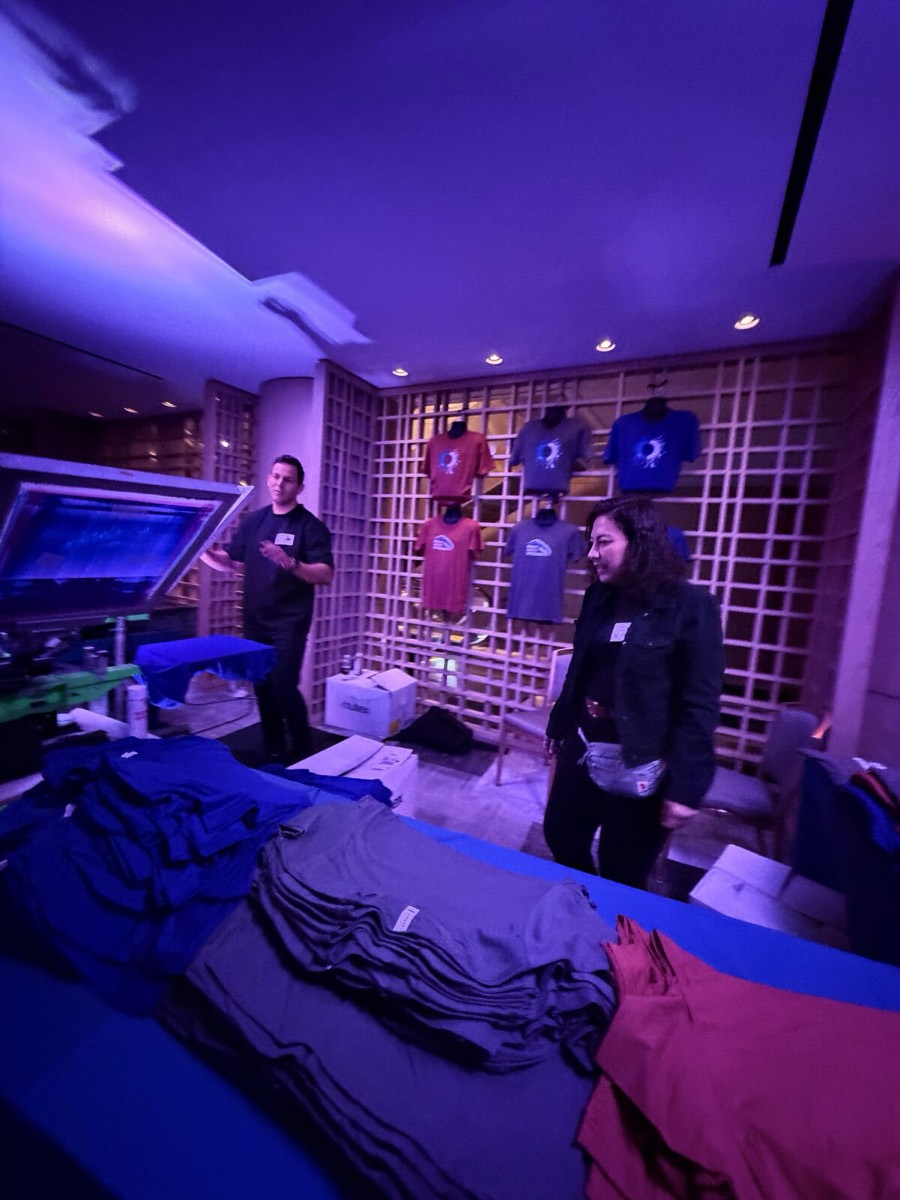 Live-printed sample shirts hanging at a Merch Troop event booth with folded stacks ready for guests