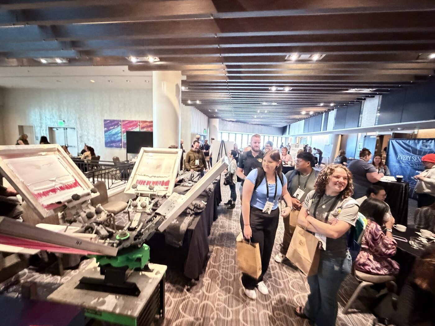 A busy expo-floor live-printing activation with crew working presses as attendees pass