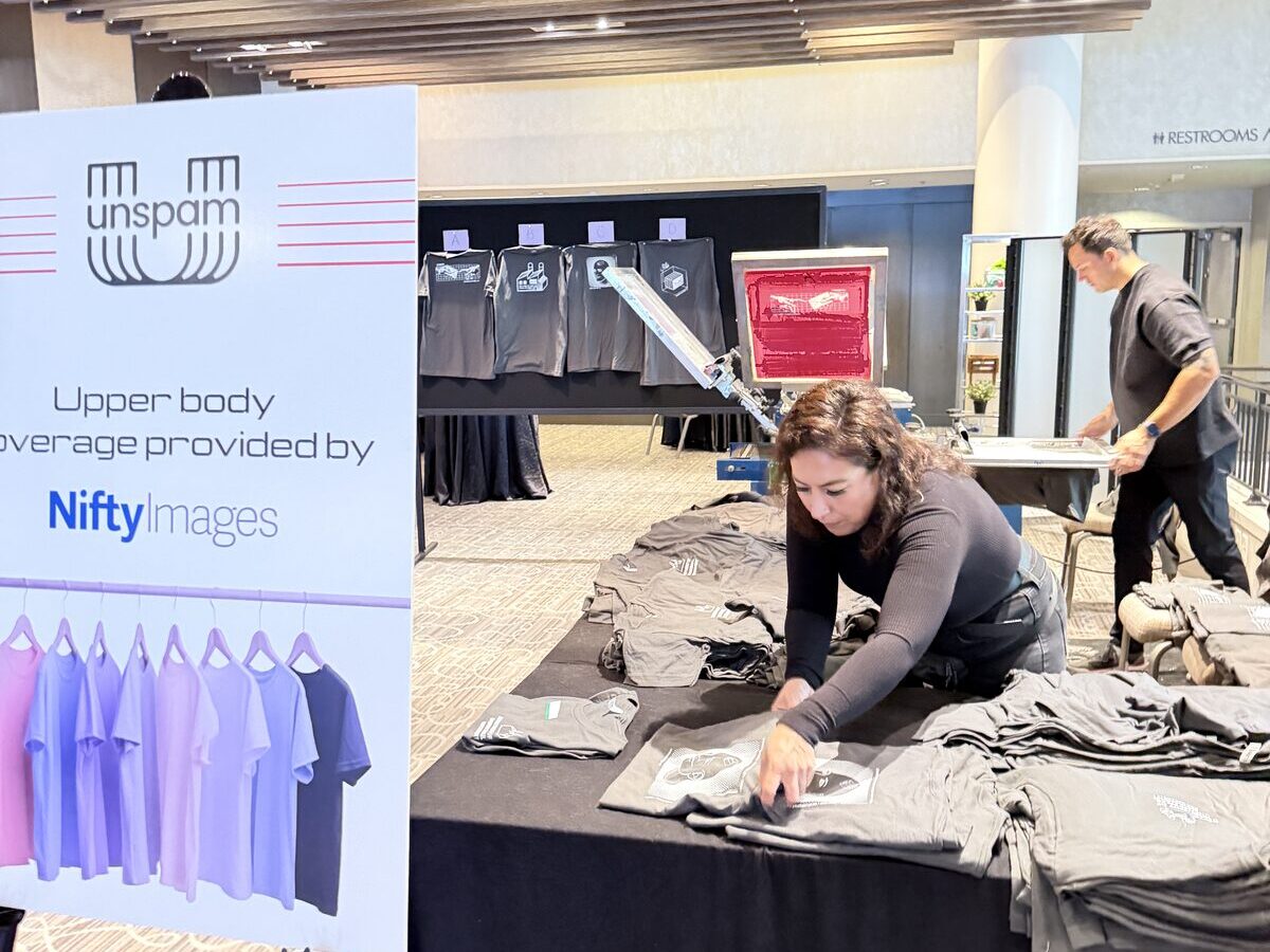 Crew member organizing folded freshly printed t-shirts at a draped event merch table