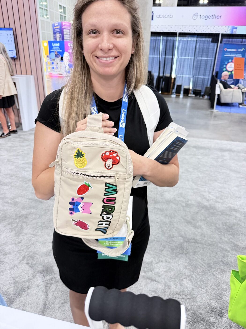 A smiling event guest holding up custom-printed tote bags at a bright booth