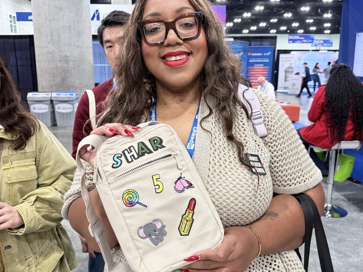Smiling guest holding a custom patch-decorated crossbody bag at an event booth