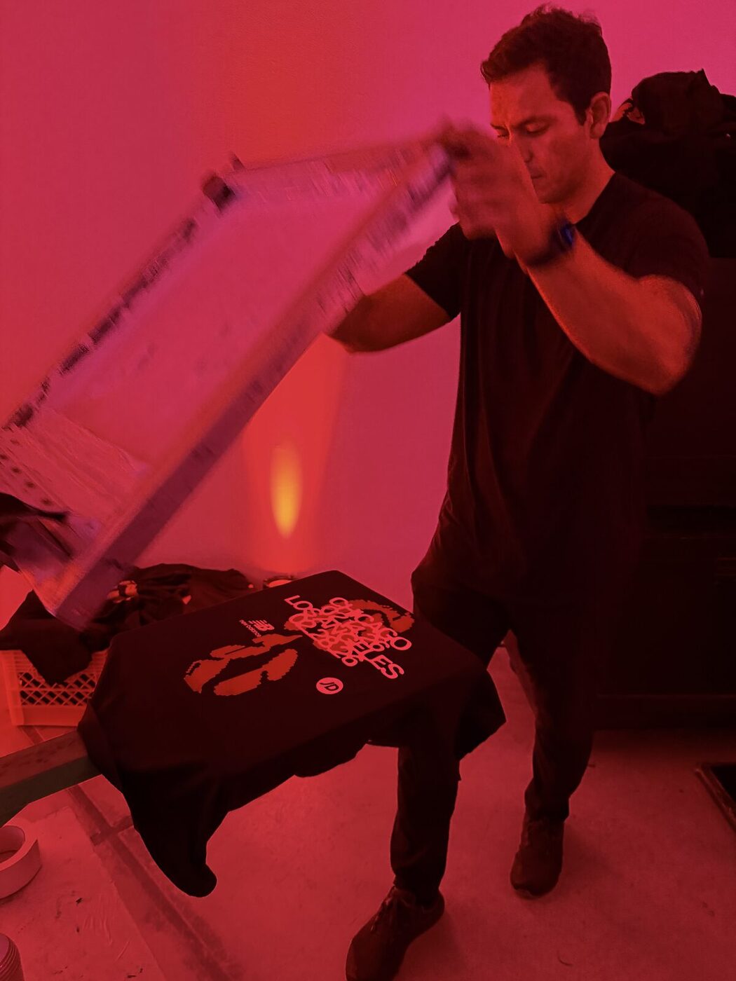 A printer pulling a squeegee across a screen under deep red event light
